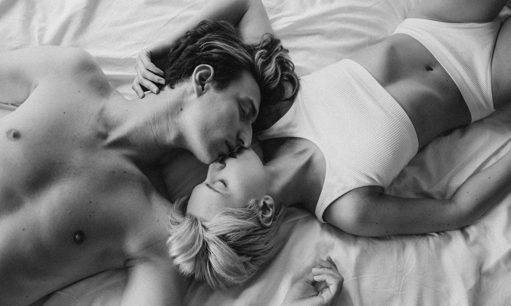 Black n white image of an erotic couple kissing on bed.